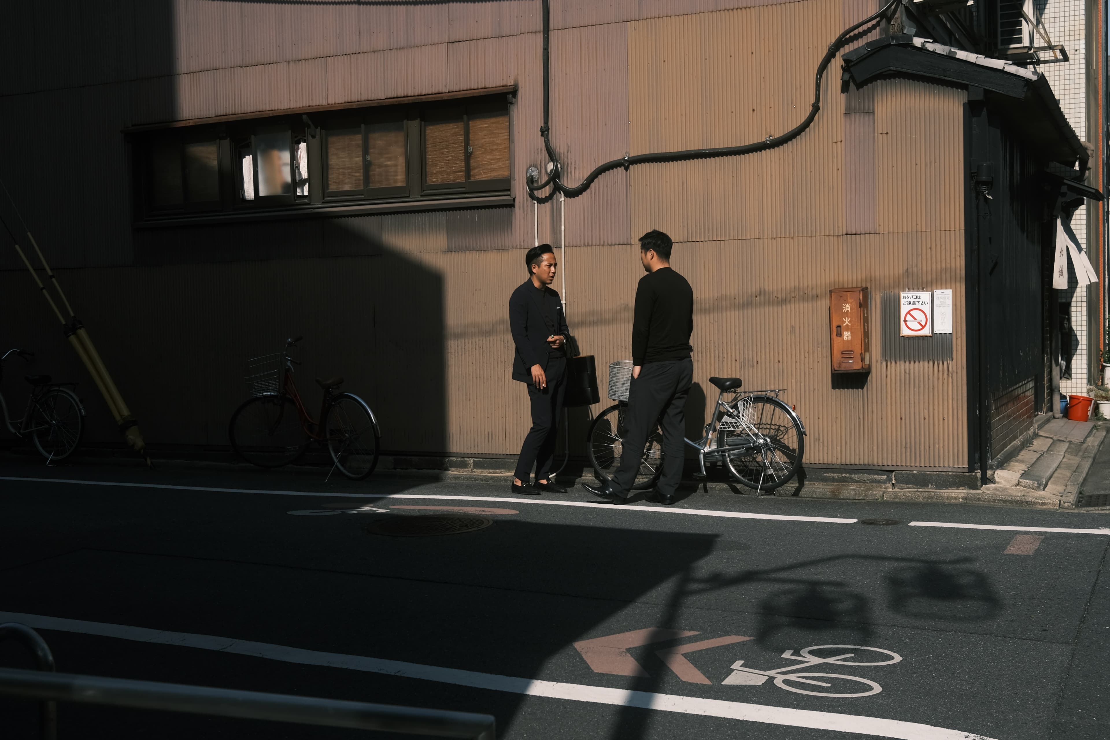 Two people talking beside a bicycle on a sunlit Tokyo street.